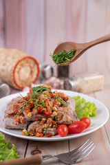 Spicy pork minced with tomatoes and lettuce on a white plate on a wooden table.
