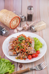 Spicy pork minced with tomatoes and lettuce on a white plate on a wooden table.