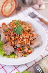 Spicy pork minced with tomatoes and lettuce on a white plate on a wooden table.