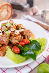 Spicy pork minced with tomatoes and lettuce on a white plate on a wooden table.