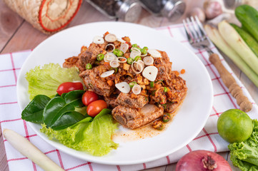 Spicy pork minced with tomatoes and lettuce on a white plate on a wooden table.