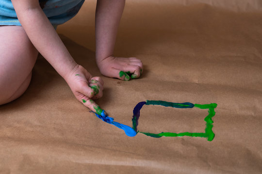 Dziecko maluje farbami obrazek na papierze przy użyciu rąk