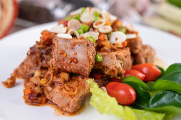 Spicy pork minced with tomatoes and lettuce on a white plate on a wooden table.