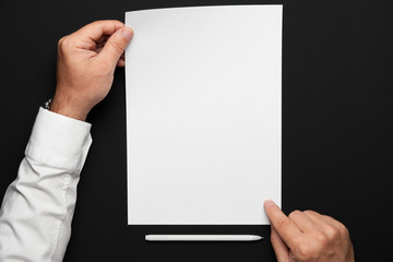 a blank sheet of paper and a businessman's hands on a black table, a white shirt and a wrist watch, a top view-a template for any text or inscription