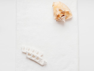 Huge natural seashell on a white towel and pedicure finger separator. Personal care at home.