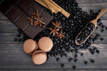 Top view of coffee beans, macarons, star anise, cinnamon stick, chocolate, on wooden table.