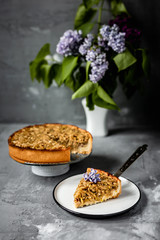 Apple pie, a piece and a full one, on grey background, a lilac bouquet, shot with natural light