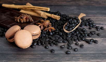 Coffee beans, macarons, star anise, dark chocolate, cinnamon stick, on wooden background.