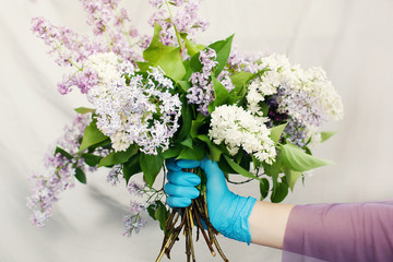 Delivery woman in medical rubber gloves holds large lilac bouquet. Online shopping, delivery service, disease outbreak, coronavirus covid-19 pandemic 