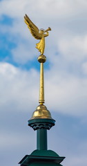 Fototapeta na wymiar Gilded angel with a trumpet on the spire of the bell tower of the Orthodox Church against the blue sky with clouds closeup