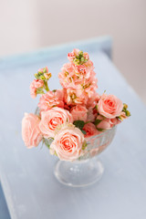 pink roses in a glass vase against the background of a vintage blue stool