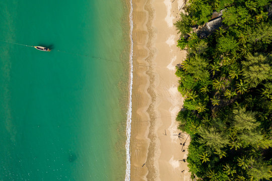 Aerial view of a beautiful, empty tropical beach surrounded by palm trees with small wooden fishing boats