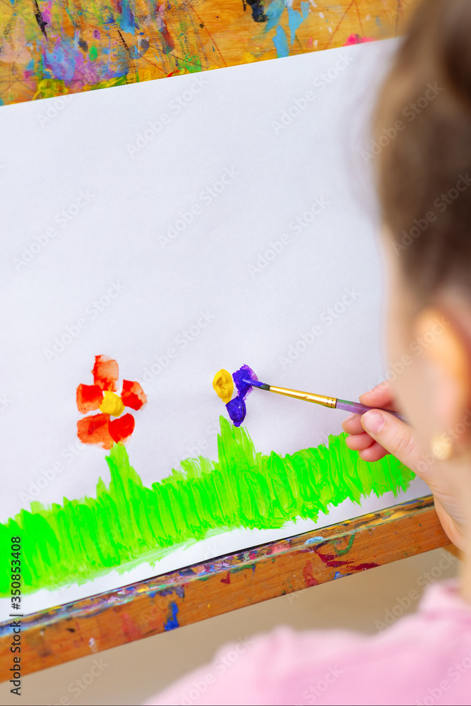 Poster hand of child drawing flowers on green grass with brush by watercolors on white paper on an easel.