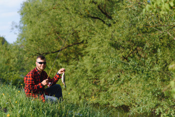 fisherman by the river with a catch of fish. Man fisherman holds in hand fish.
