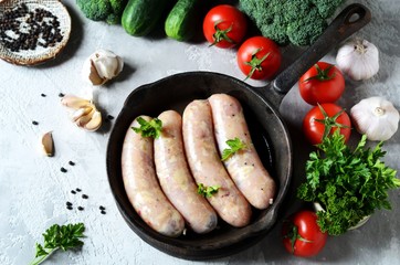 Raw homemade sausages (chicken, turkey) in a pan on a gray background with vegetables. Still life