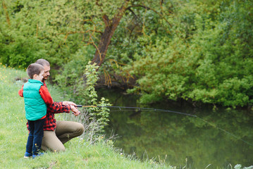 A father teaching his son how to fish on a river outside in summer sunshine