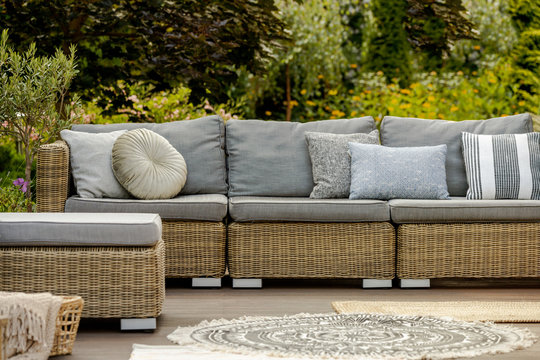 Grey pillows on trendy wicker L shape sofa in the green garden