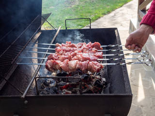 Shashlik or shashlyk preparing on a barbecue grill over charcoal. Grilled cubes of pork meat on metal skewer. Outdoor.