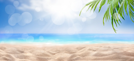 A summer vacation, holiday background of a tropical beach, blue sea, white clouds, sun flare and green palm tree leaves.