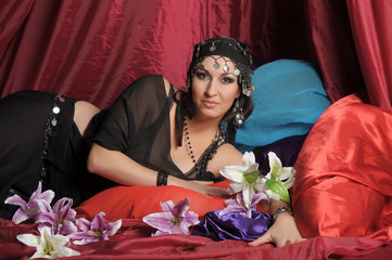 eastern woman in black clothes lies on pillows