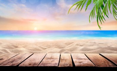 A wooden table product display with a summer vacation, holiday background of a tropical beach and blue sea at sunset with the sun on the horizon with bokeh and palm trees.
