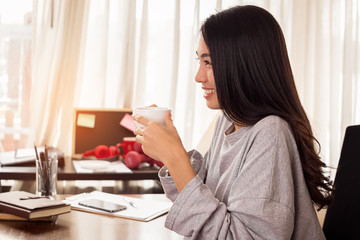 Young Asian woman is working and drinking coffee at home. work at home concept.