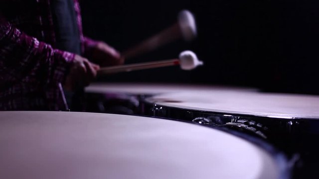 A man playing timpani in a dark room, close up.