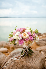 beautiful wedding bouquet in violet and white tones of roses and eustoma, photographed on stones by the sea