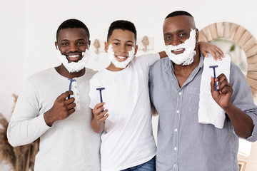 Three generational men family shaving together in bathroom and smiling at camera