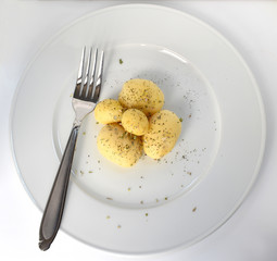 Boiled peeled potatoes on a white plate with a fork, potatoes with spices and greens