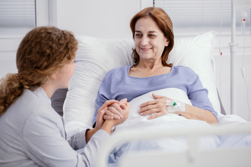 Smiling elderly woman and caring nurse holding her hand in the hospice