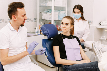 A beautiful girl sits in the dentist's chair and listens to the doctor and his assistant. Dentist appointment and dental health care