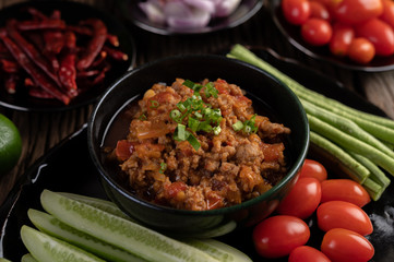 Sweet pork in a black bowl, complete with cucumbers, long beans, tomatoes, and side dishes