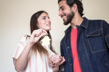 Happy couple in the new apartment . The woman is having the key to a house. Key with a keychain in the shape of the house. Focus on hand - Image