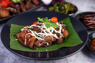 Fried pork topped with sesame seeds put on a banana leaf in a black dish.
