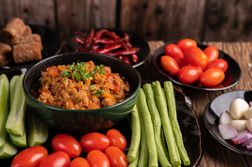 Sweet pork in a black bowl, complete with cucumbers, long beans, tomatoes, and side dishes