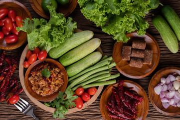 Sweet pork in a wooden bowl with cucumber, long beans, tomatoes, and side dishes.