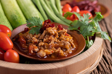 Sweet pork in a wooden bowl with cucumber, long beans, tomatoes, and side dishes.