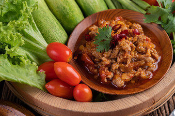 Sweet pork in a wooden bowl with cucumber, long beans, tomatoes, and side dishes.