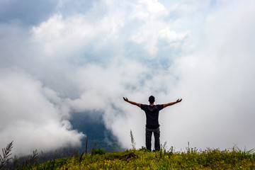 Fototapeta na wymiar man isolated feeling the serene nature at hill top with amazing cloud layers in foreground