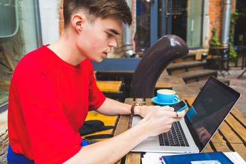 Hipster guy using apps on mobile phone during online training course on laptop computer while resting in coffee shop during free time