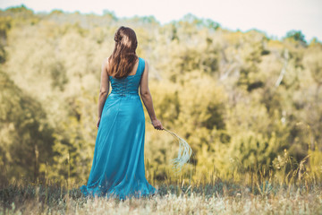 beautiful romantic girl enjoying nature with fluffy feather grass in hands, young elegant woman looking into the distance, bride in blue long dress