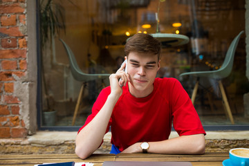 Smiling man with good mood talking via mobile phone while sitting in coffee shop outdoors during...