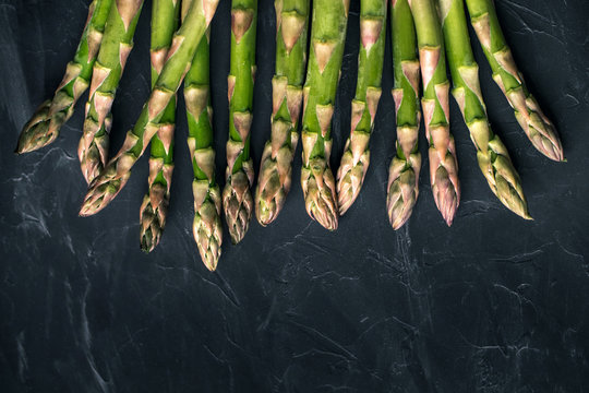Fresh green uncooked asparagus lies on black textured background. Healthy raw green food. Raw of asparagus stalks at the top of the picture