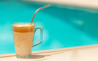 Greek coffee drink called frappe coffee at the edge of a swimming pool (selected focus)