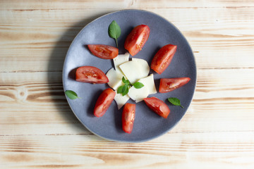 Plate with cheese, tomato slices, basil leaves on wooden background