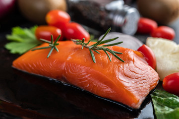 Raw salmon fillets, pepper, kiwi, pineapples, and rosemary onto a plate and black cement floor.