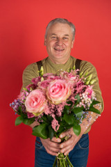 An elderly man with a large beautiful bouquet of flowers stands on a red background, the concept of a holiday and a happy old age