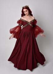 Portrait of a beautiful woman with red hair wearing  a  flowing Burgundy fantasy gown and golden crown.  full length standing pose, isolated against a studio background  © faestock