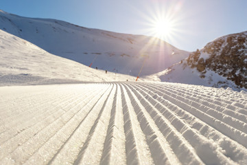 Close-up straight line rows of freshly prepared groomed ski slope piste with bright shining sun and...